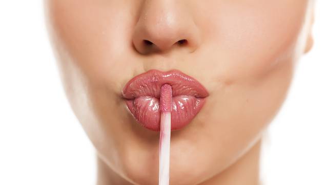 young beautiful woman apply a lip gloss on her lips on white background