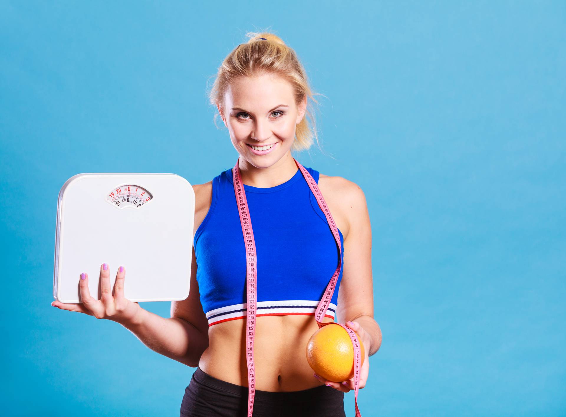 Žena drži vagu, metar i naranču - gubitak težine