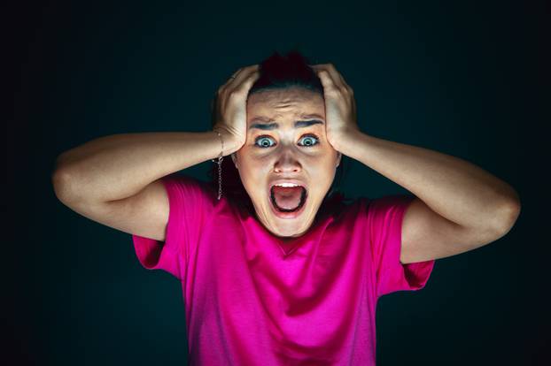 Close up portrait of young crazy scared and shocked woman isolated on dark background