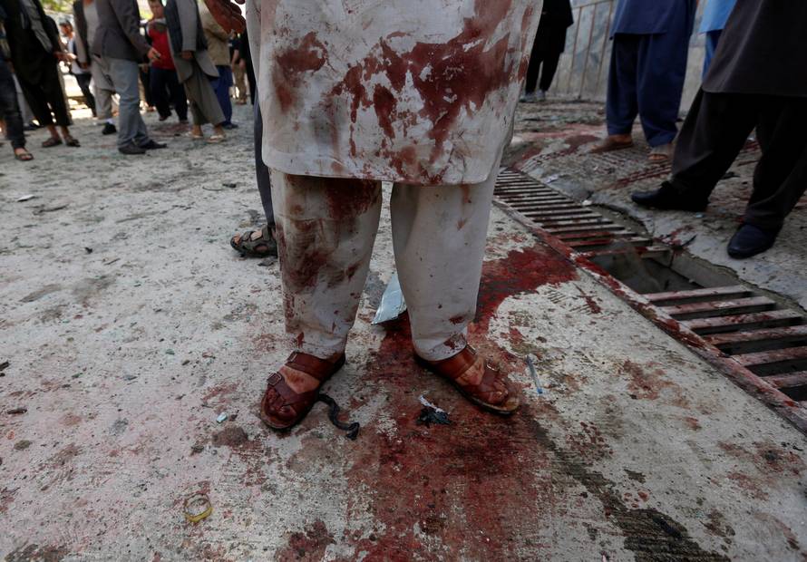 A man stained with blood inspects at the site of a suicide bomb attack in Kabul