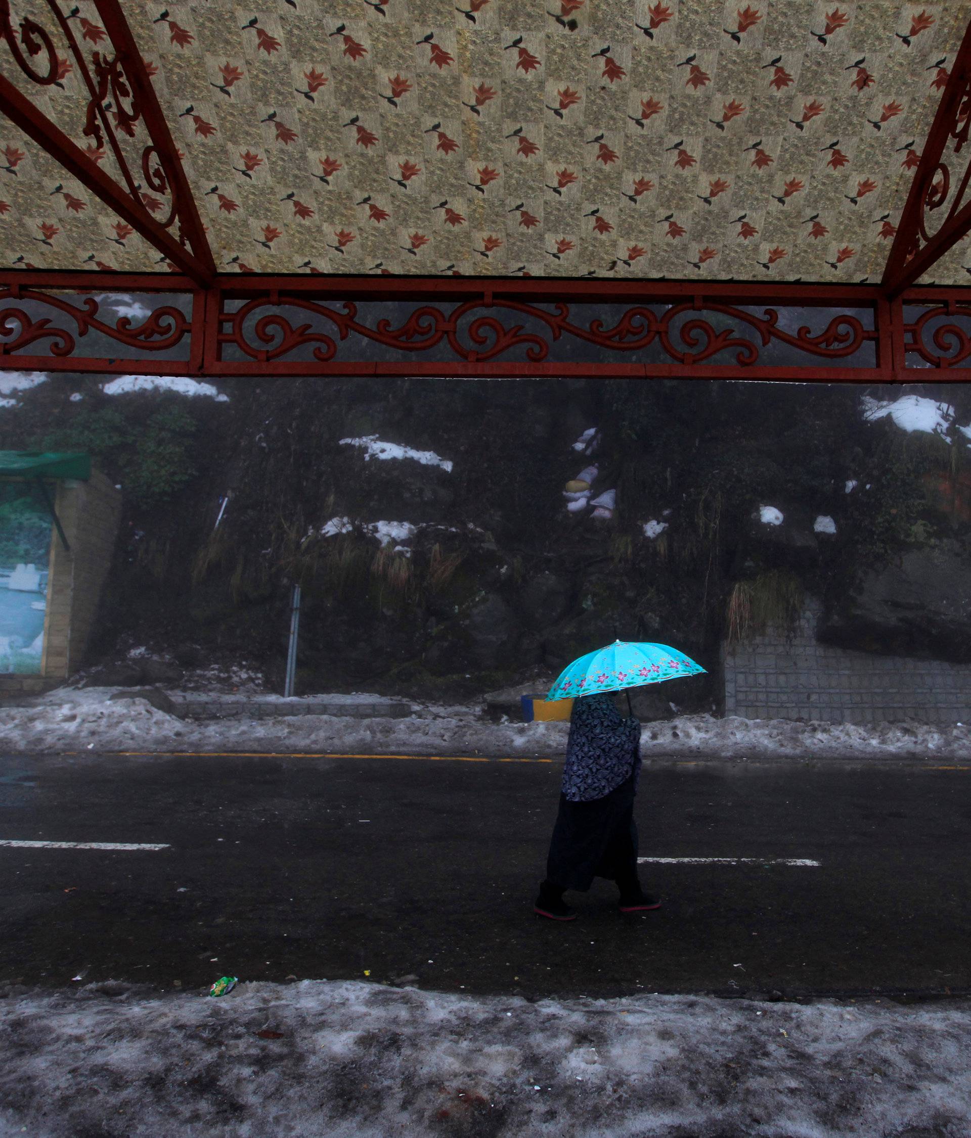 A woman holds an umbrella as she walks on a road during a cold winter day after snow fall in the hill-resort town of Murree, northeast of capital Islamabad