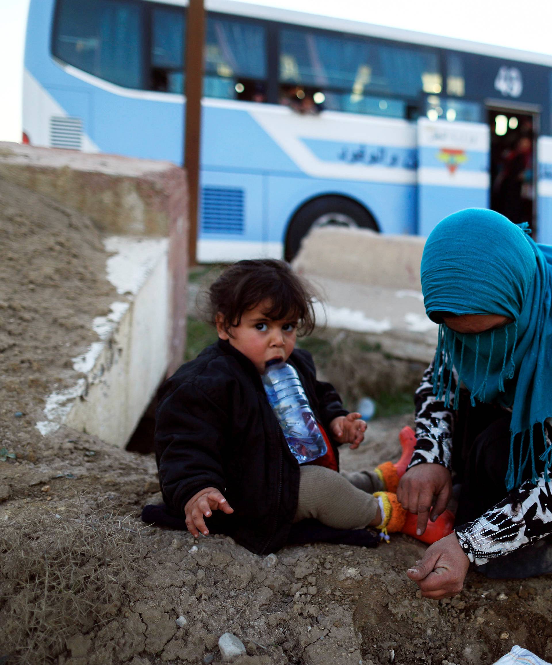 A woman, who just fled a village controled by Islamic State militants, checks her daughter as she sits in front of a bus before heading to the camp at Hammam Ali, south of Mosul