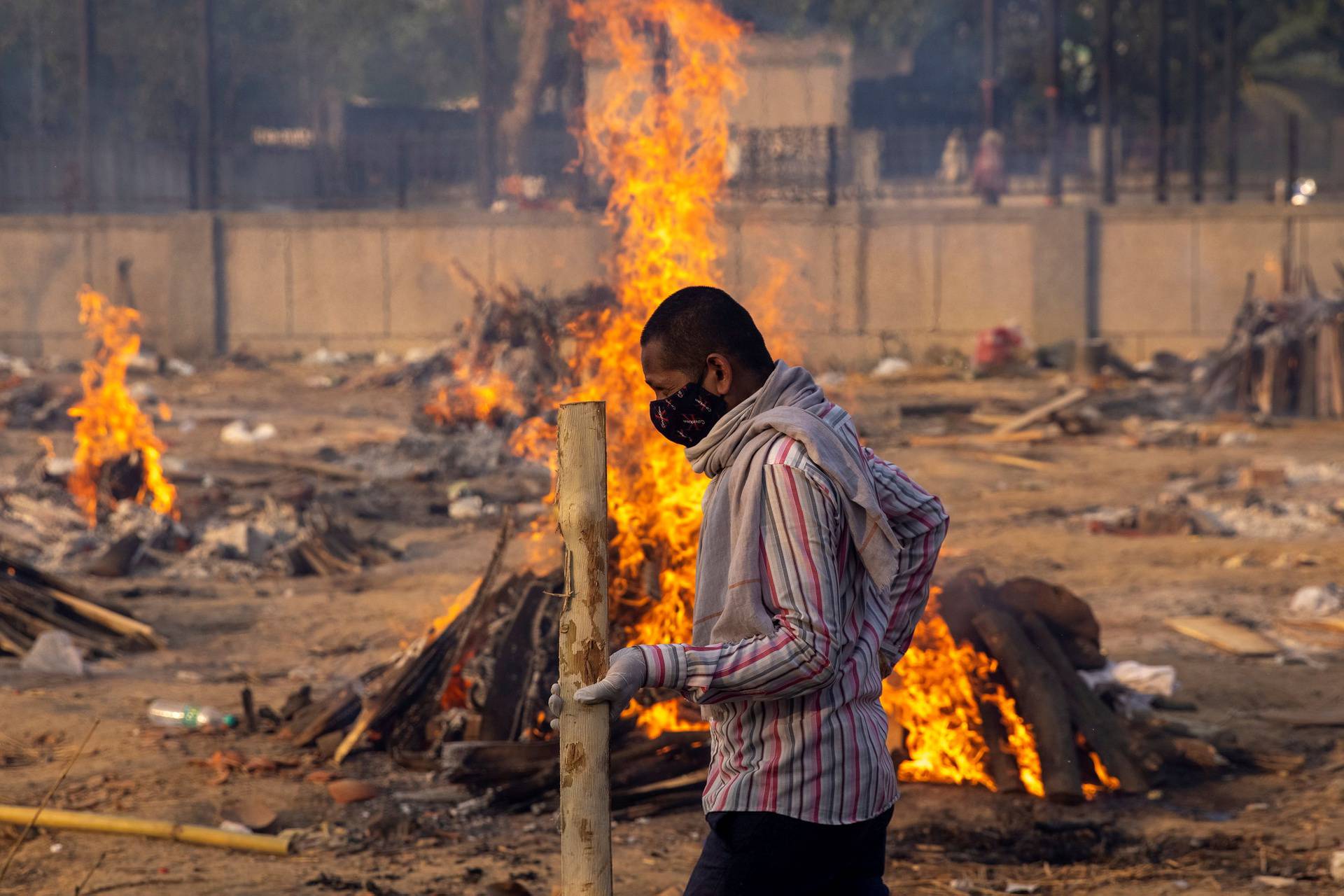 A man walks past burning funeral pyres of people, who died due to the coronavirus disease (COVID-19), at a crematorium ground in New Delhi