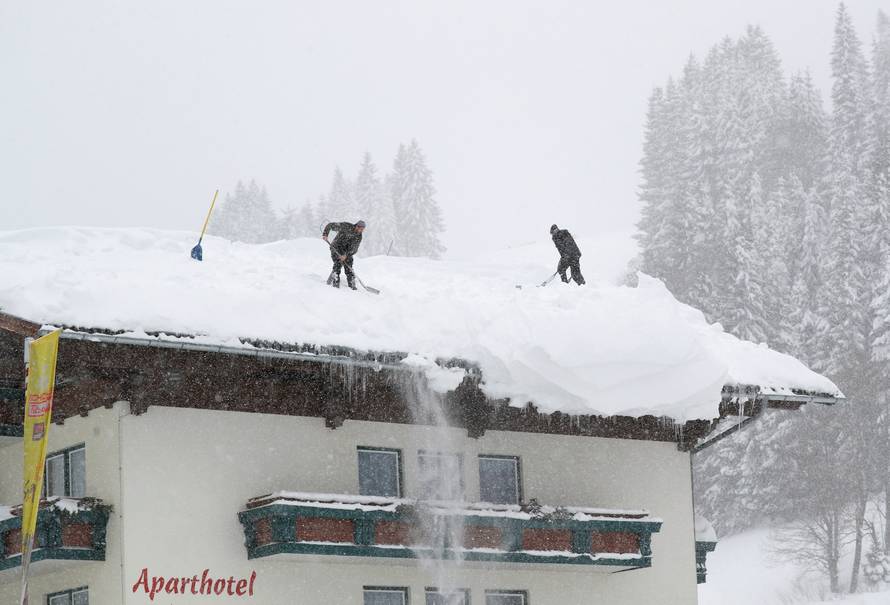 Two men shovel snow on a rooftop during heavy snowfall in Filzmoos
