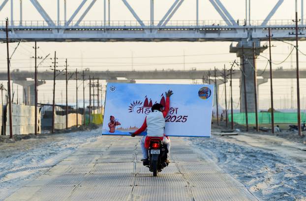 A man commutes on a motorcycle as he carries a large hoarding board that reads "Maha Kumbha 2025" ahead of the "Kumbh Mela", or the Pitcher Festival, in Prayagraj