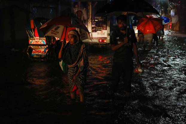 A woman wades through water as streets are flooded due to continuous rain, before the Cyclone Sitrang hits in Dhaka