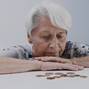 Sad face expression of old gray haired woman looking in few coins left on the table