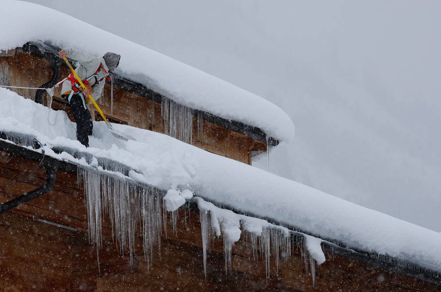 A man shovels snow on a rooftop during heavy snowfall in Flachau