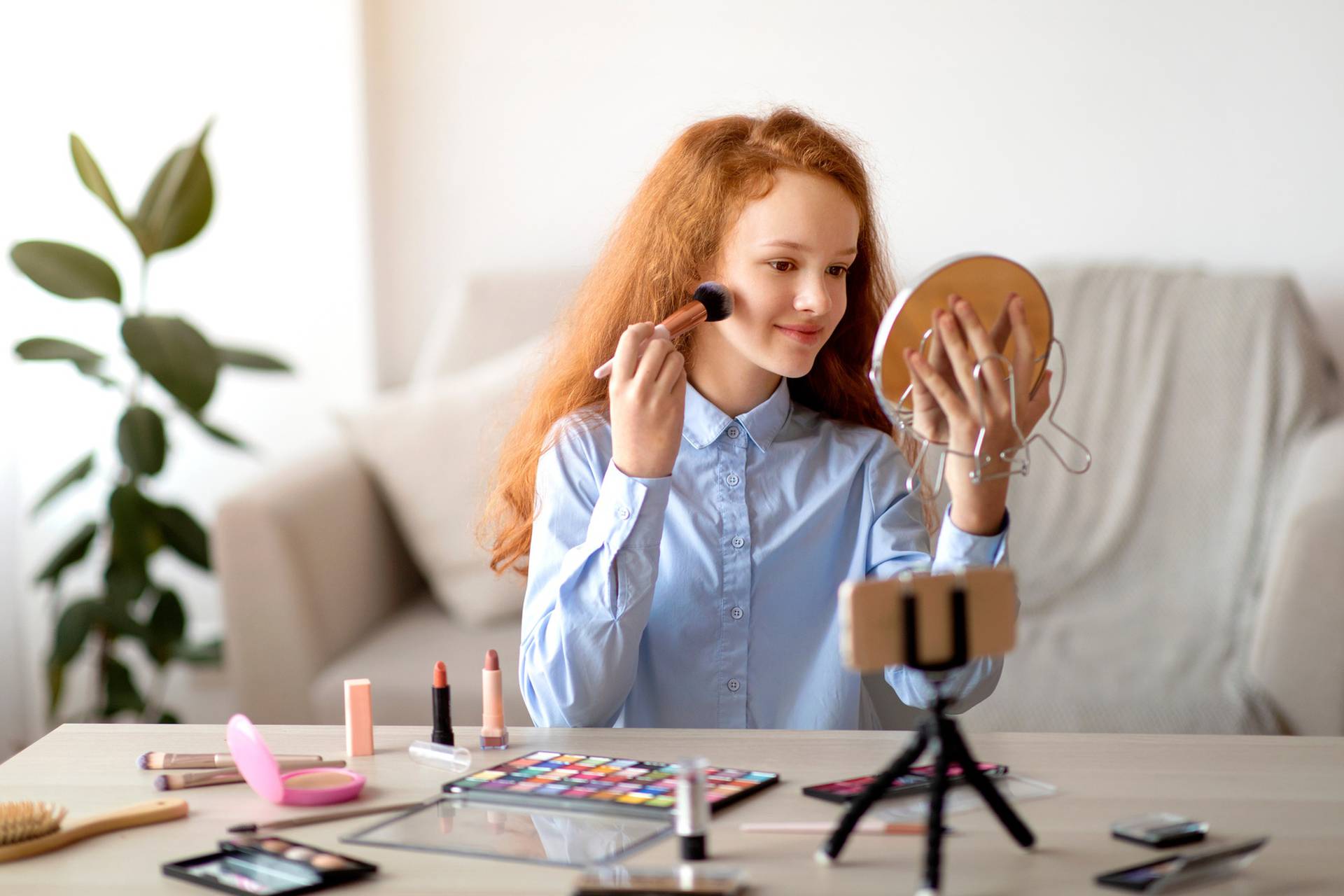 Teen applying face powder, recording beauty blog on smartphone