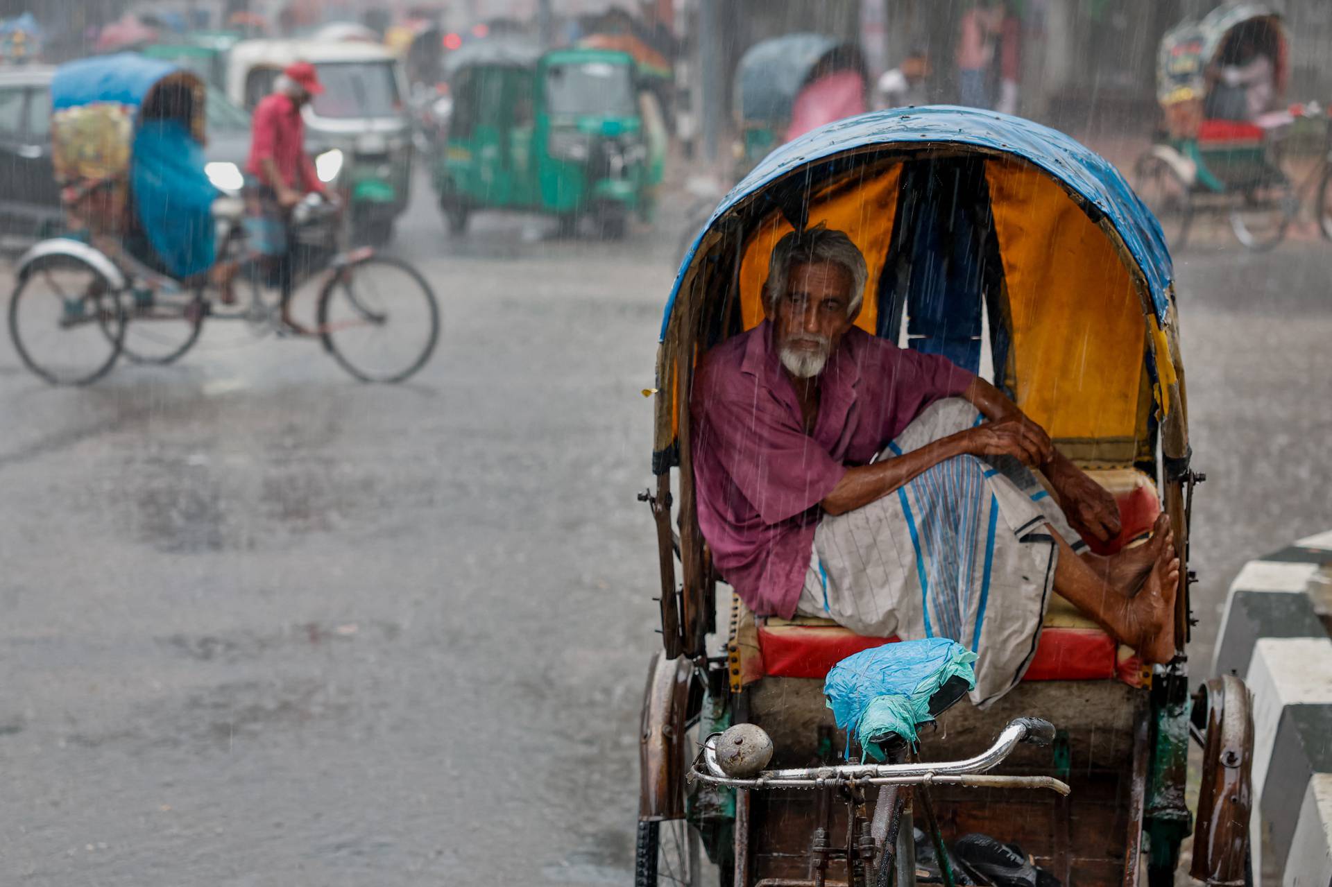 A rickshaw driver sits inside his rickshaw to take cover from rain during a downpour in Dhaka