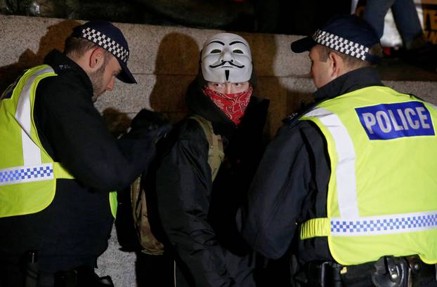 Police officers search a protester during the "Million Mask March" in London