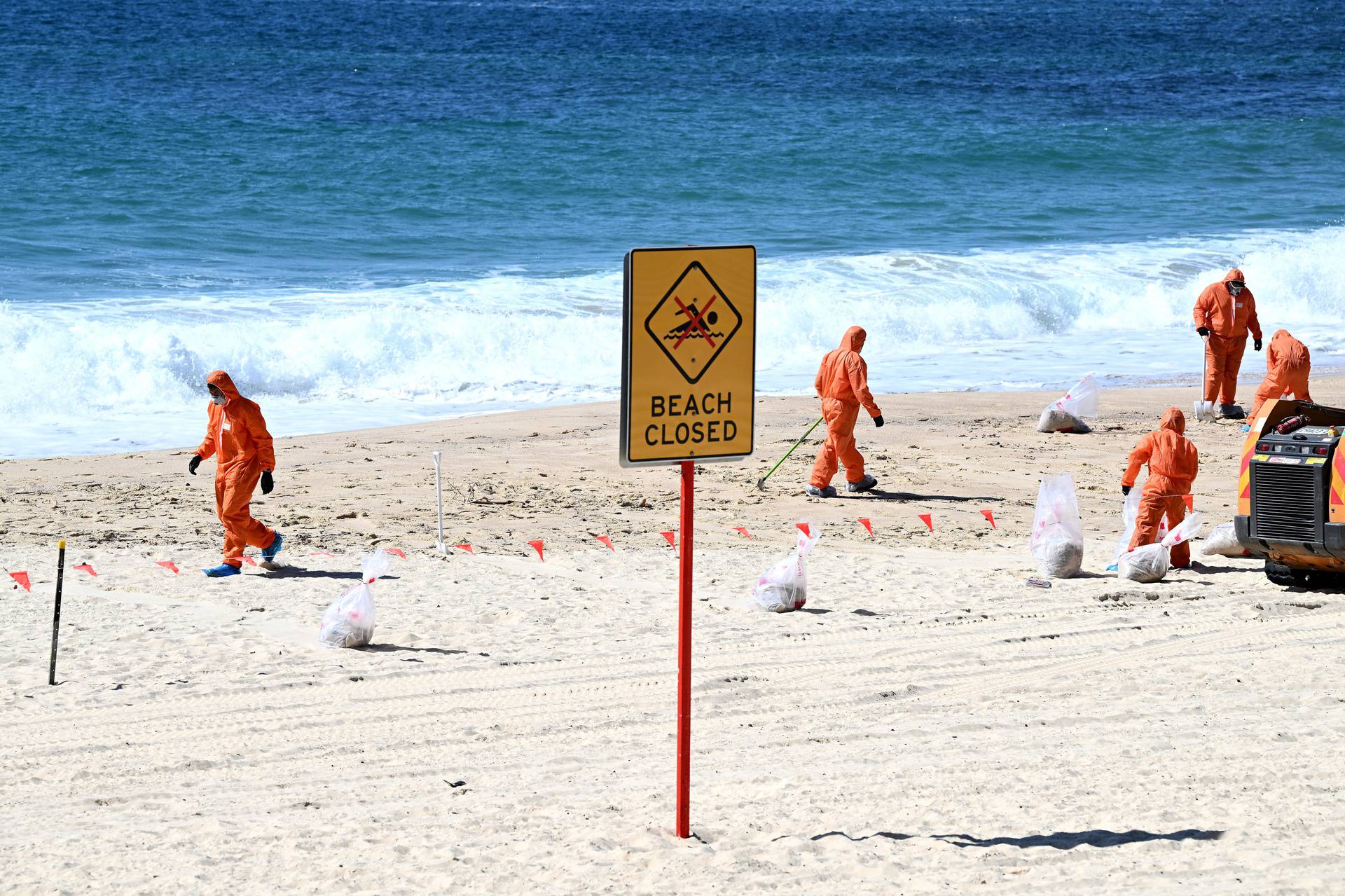 Workers in protective clothing clean up unknown debris washed up on Coogee Beach