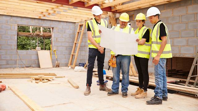 Builder,On,Building,Site,Looking,At,Plans,With,Apprentices