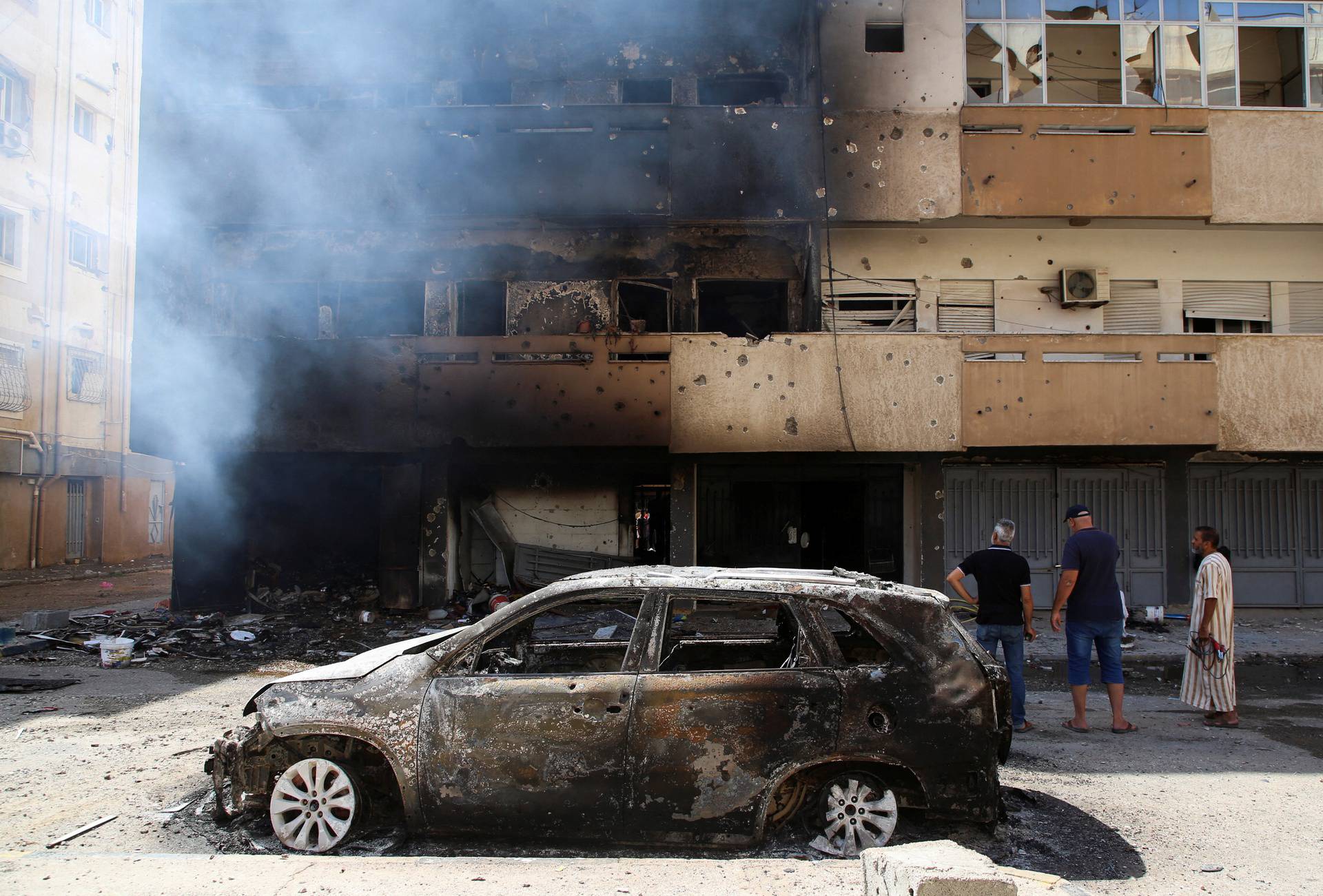 Men looks at a building burning after yesterday's clashes in Tripoli