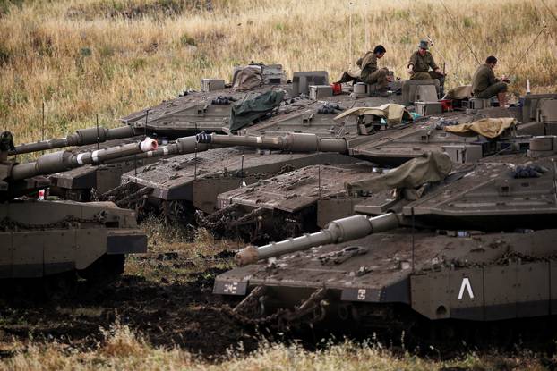 Israeli soldiers sit on tanks near the Israeli side of the border with Syria in the Israeli-occupied Golan Heights