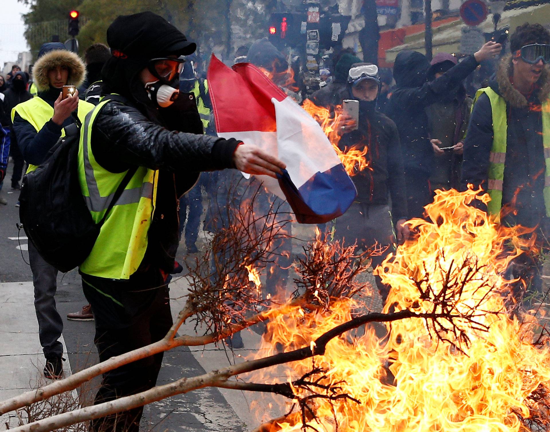 A protester wearing a yellow vest burns a French flag at a barricade during clashes with police as part of a national day of protest by the "yellow vests" movement in Paris