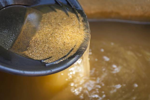 Close up of gold panning pan with sifting sand. Shallow depth of field with focus on sand flowing over edge of pan into water.
