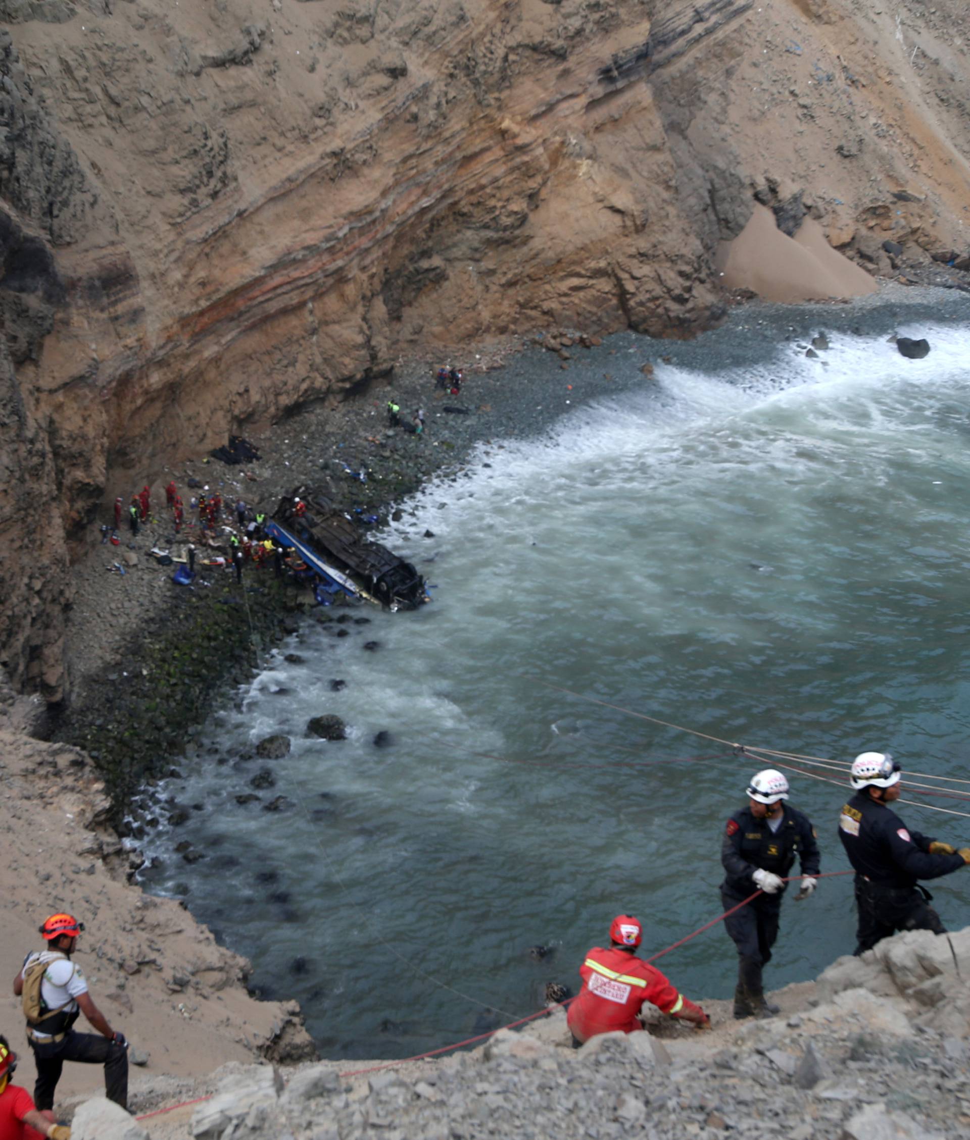 Rescue workers  and police work at the scene after a bus crashed with a truck and careened off a cliff along a sharply curving highway north of Lima