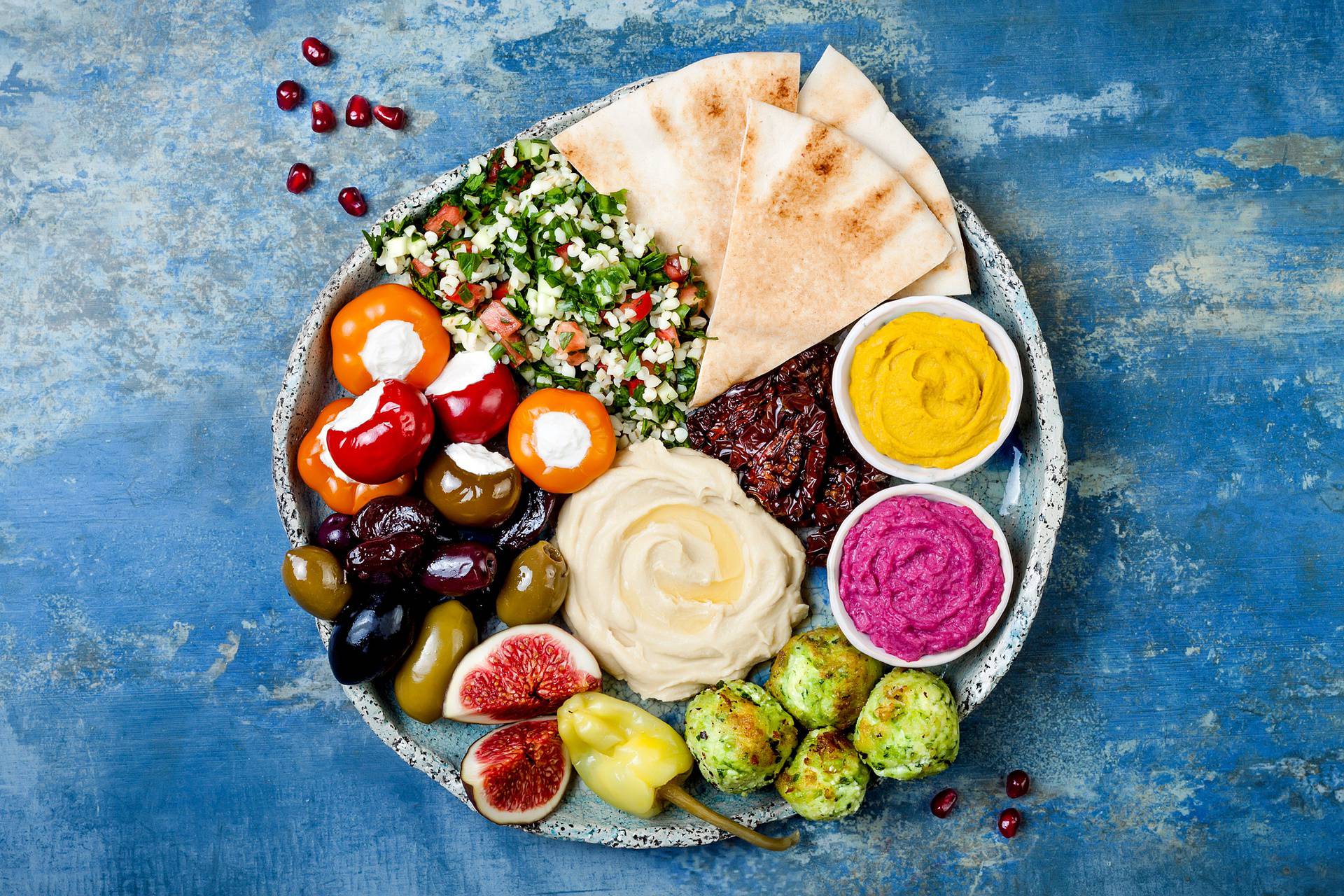 Middle Eastern meze platter with green falafel, pita, sun dried tomatoes, pumpkin and beet hummus, olives, stuffed peppers, tabbouleh, figs. Mediterranean appetizer party idea