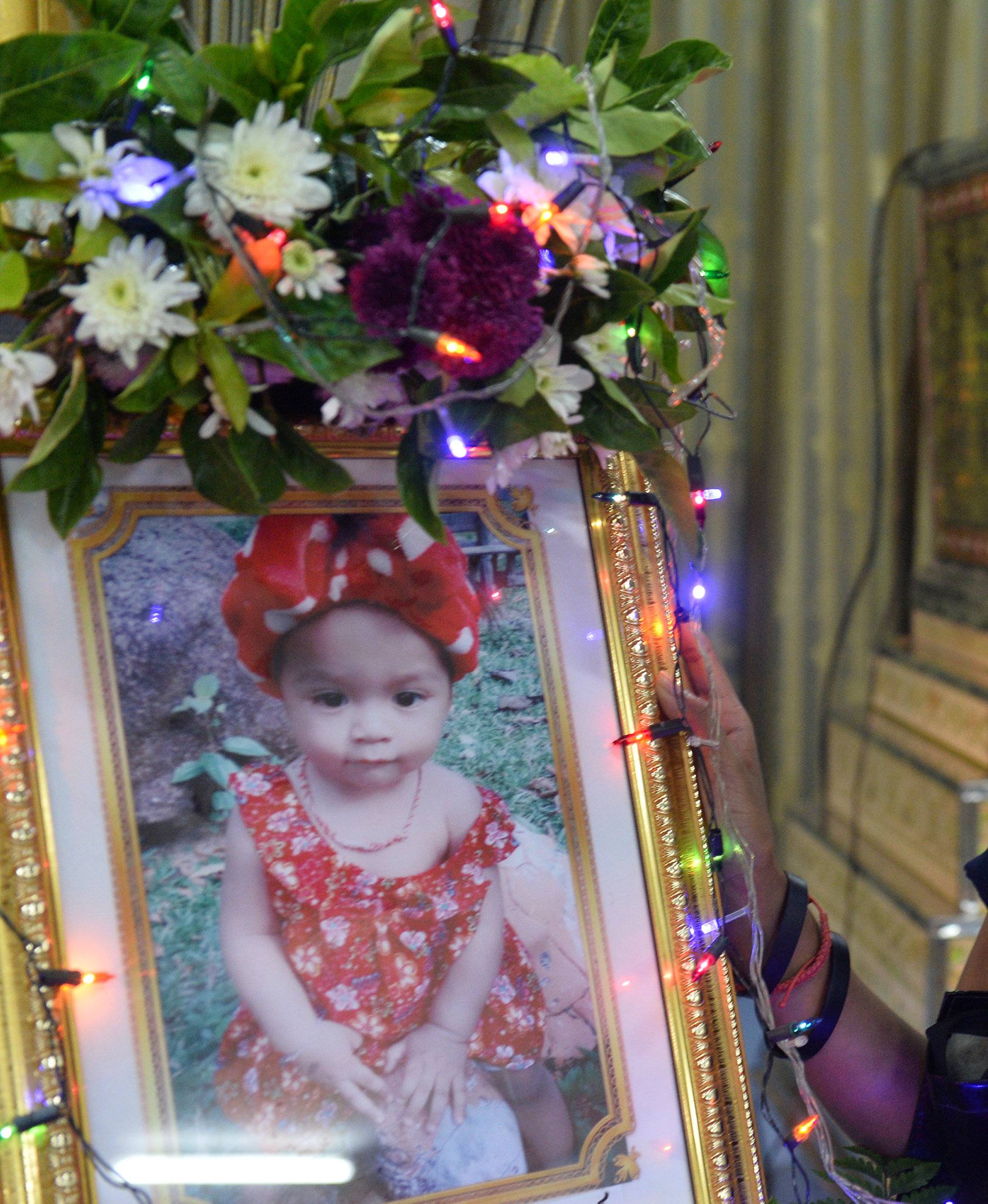 Jiranuch Trirat, mother of 11-month-old daughter who was killed by her father, stands next to a picture of her daughter at a temple in Phuket