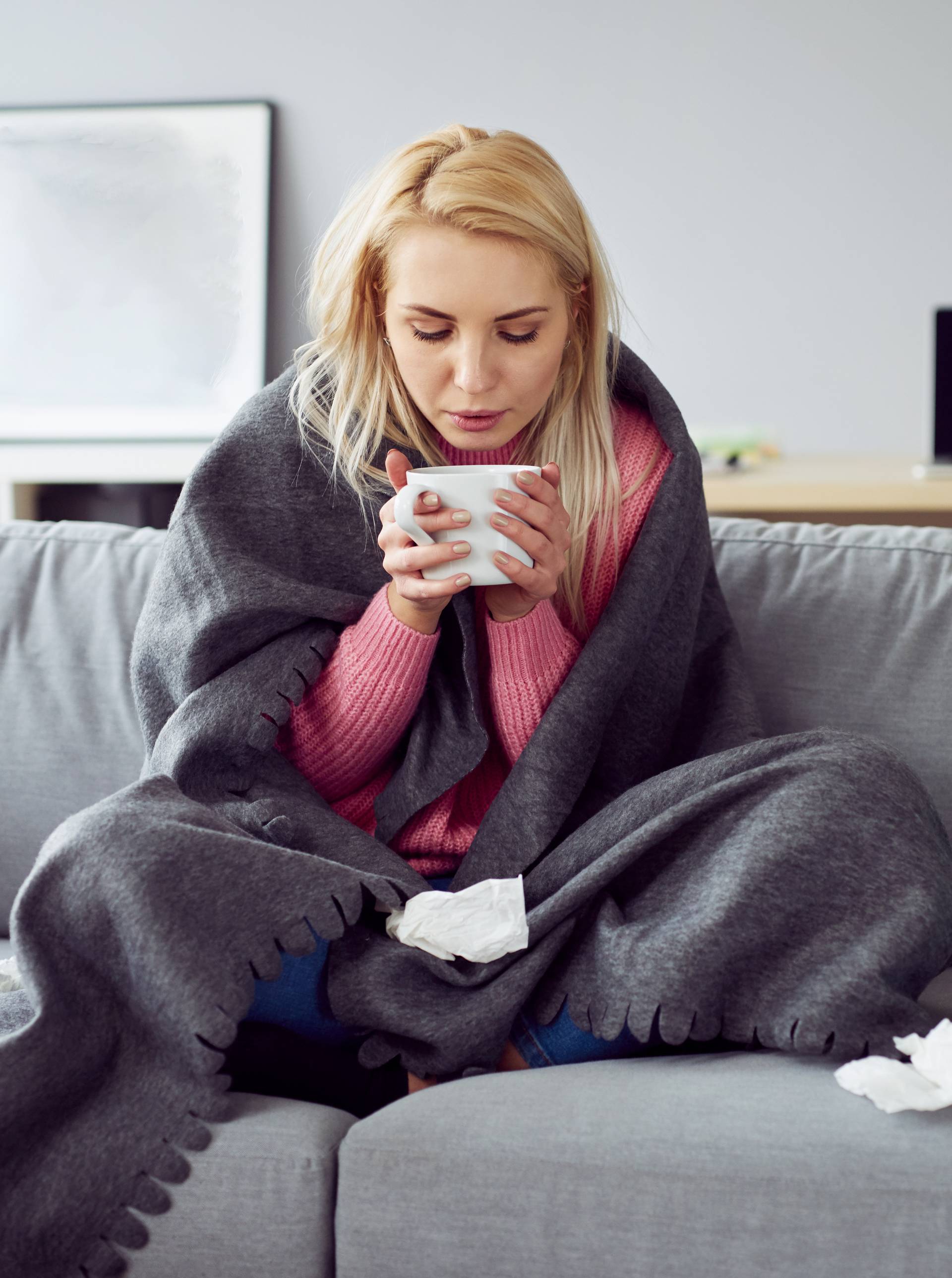 Young sick woman sitting on sofa drinking tea