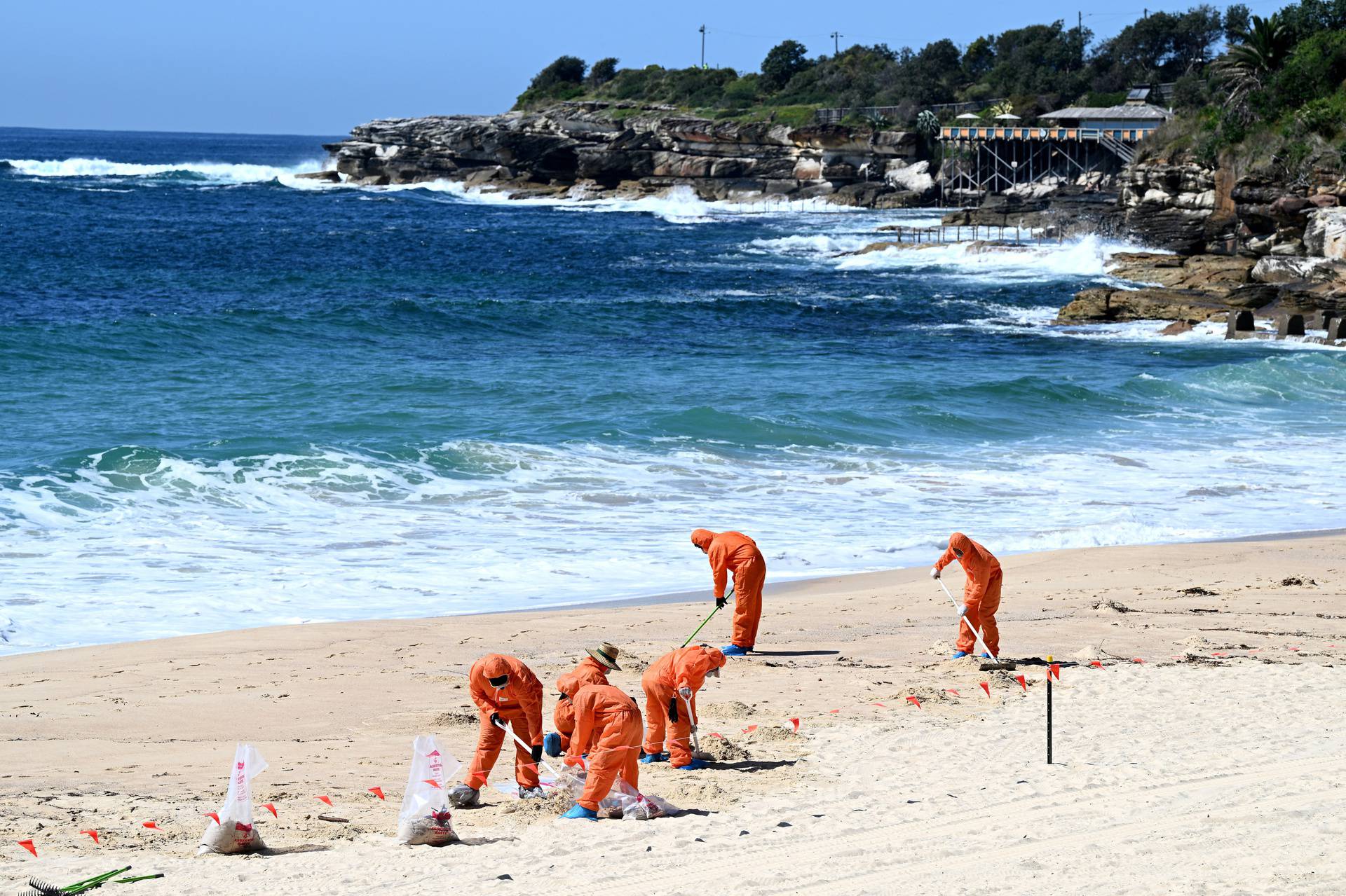 Workers in protective clothing clean up unknown debris washed up on Coogee Beach