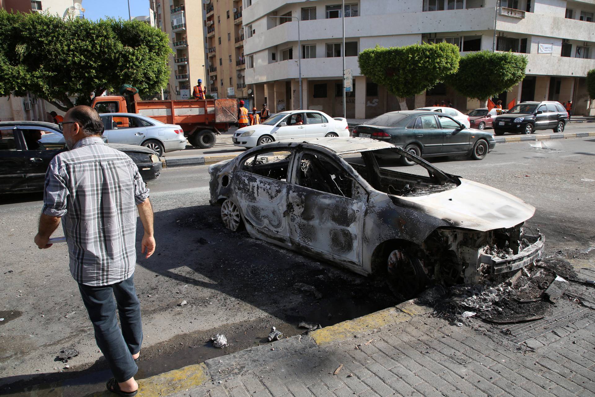 A man walks next to a burned car after yesterday's clashes in Tripoli