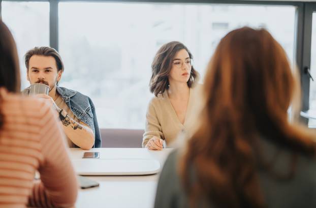 Young adults engage in a casual business discussion in a bright, contemporary office setting, conveying teamwork and collaboration.