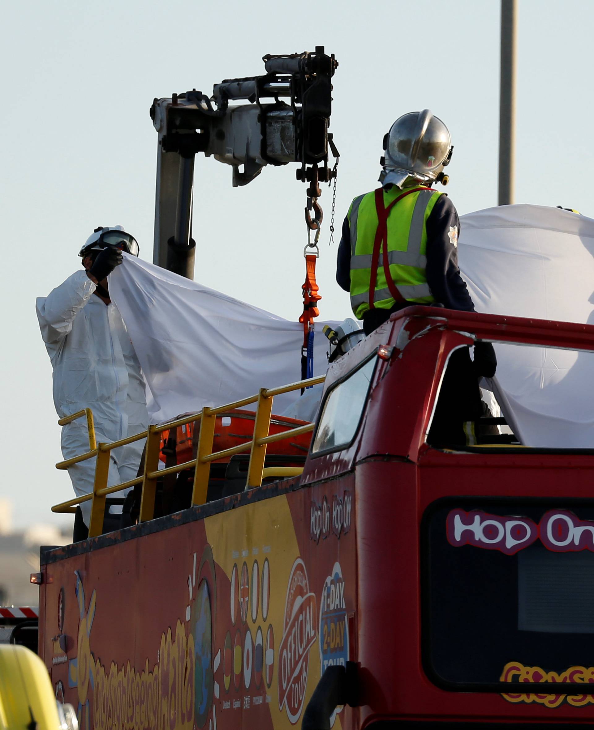 Rescue workers retrieve a tourist's body from the top of an open top, double-decker sightseeing bus after it crashed into some low-lying tree branches, in Zurrieq