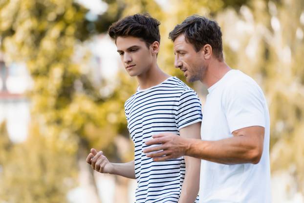 Father,Gesturing,And,Talking,With,Teenager,Son,In,Park