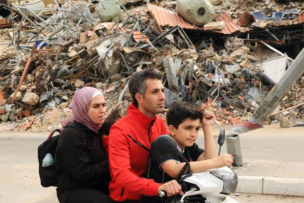 A family rides past a damaged building as they return to their home, after a 10-day ceasefire between Lebanon and Israel went into effect, in the southern suburbs of Beirut