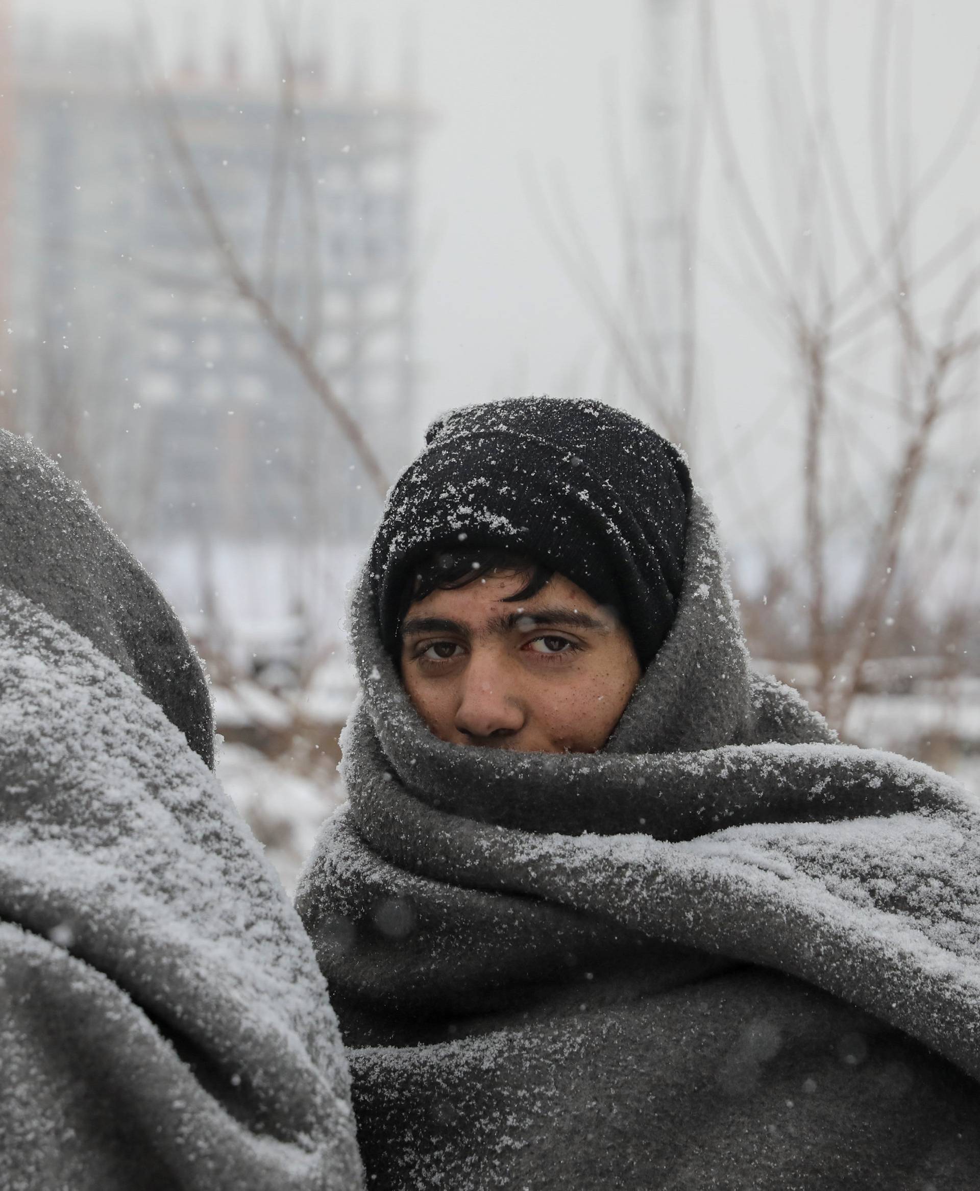 Migrants wait in line to receive free food during a snowfall outside a derelict customs warehouse in Belgrade