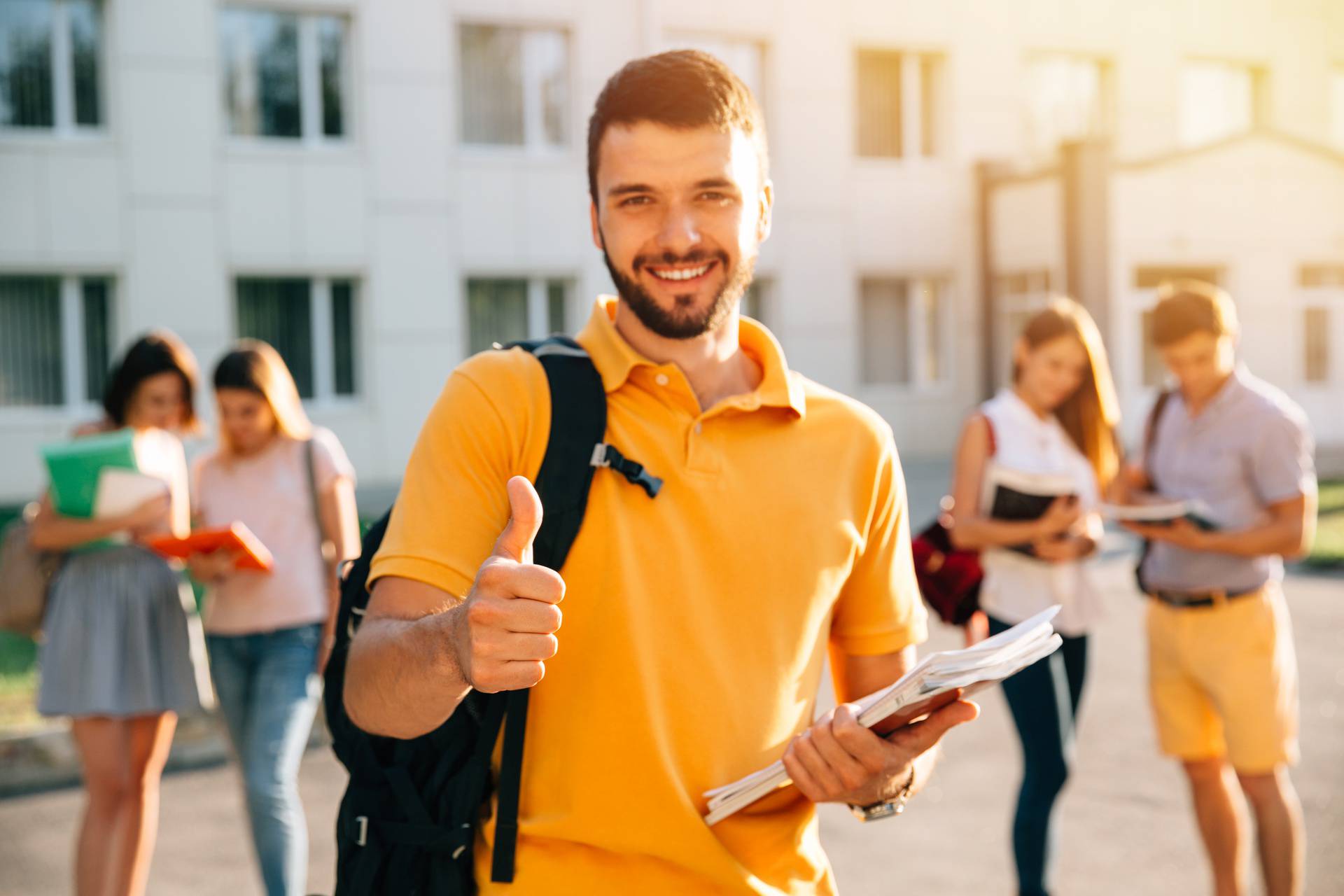 Young attractive smiling student showing thumb up outdoors on campus at the university