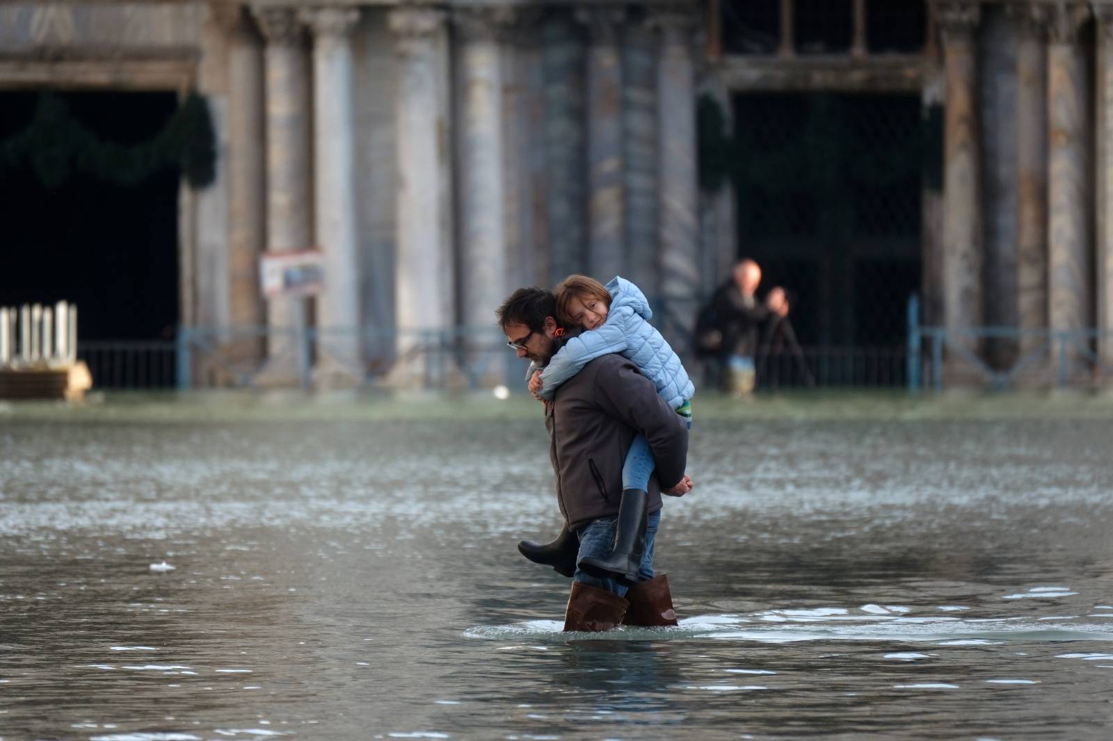 A man carries a child as he walks in the flooded St. Mark's Square during high tide in Venice