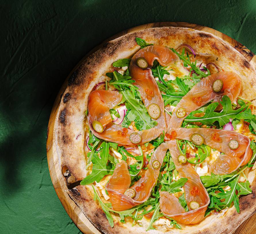 Unique pizza topped with smoked salmon and arugula on wooden board