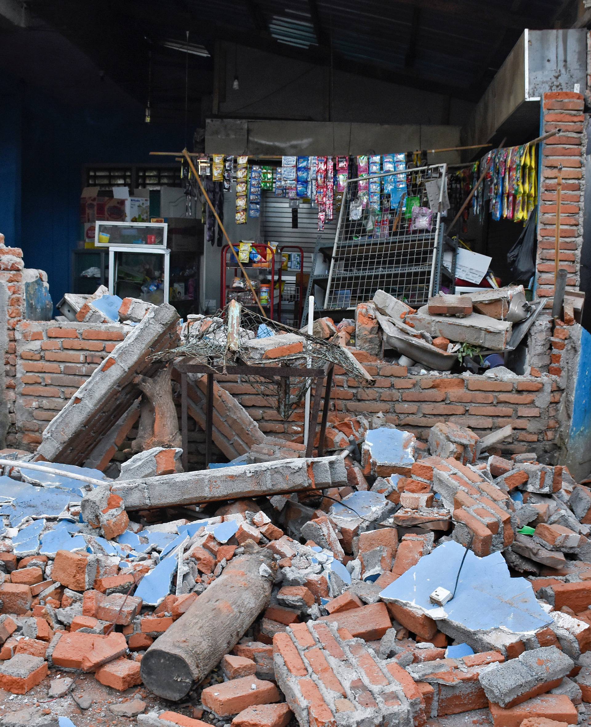 A woman walks past debris from a collapsed wall following a strong earthquake in Lendang Bajur Hamlet, Lombok