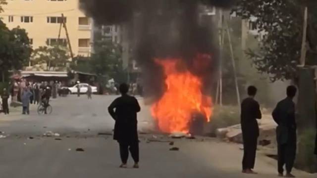 People gather around remnants of flames from cars where rockets towards Kabul's international airport were fired from but were intercepted by a missile defense system in Kabul