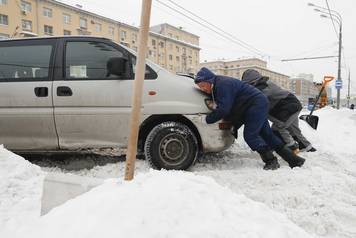 Men push a car after a heavy snowfall in Moscow