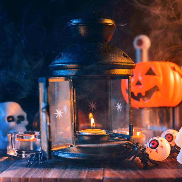 Halloween concept, spooky decorations with lighting up candle and candle holder with blue tone smoke around on a dark wooden table, close up.