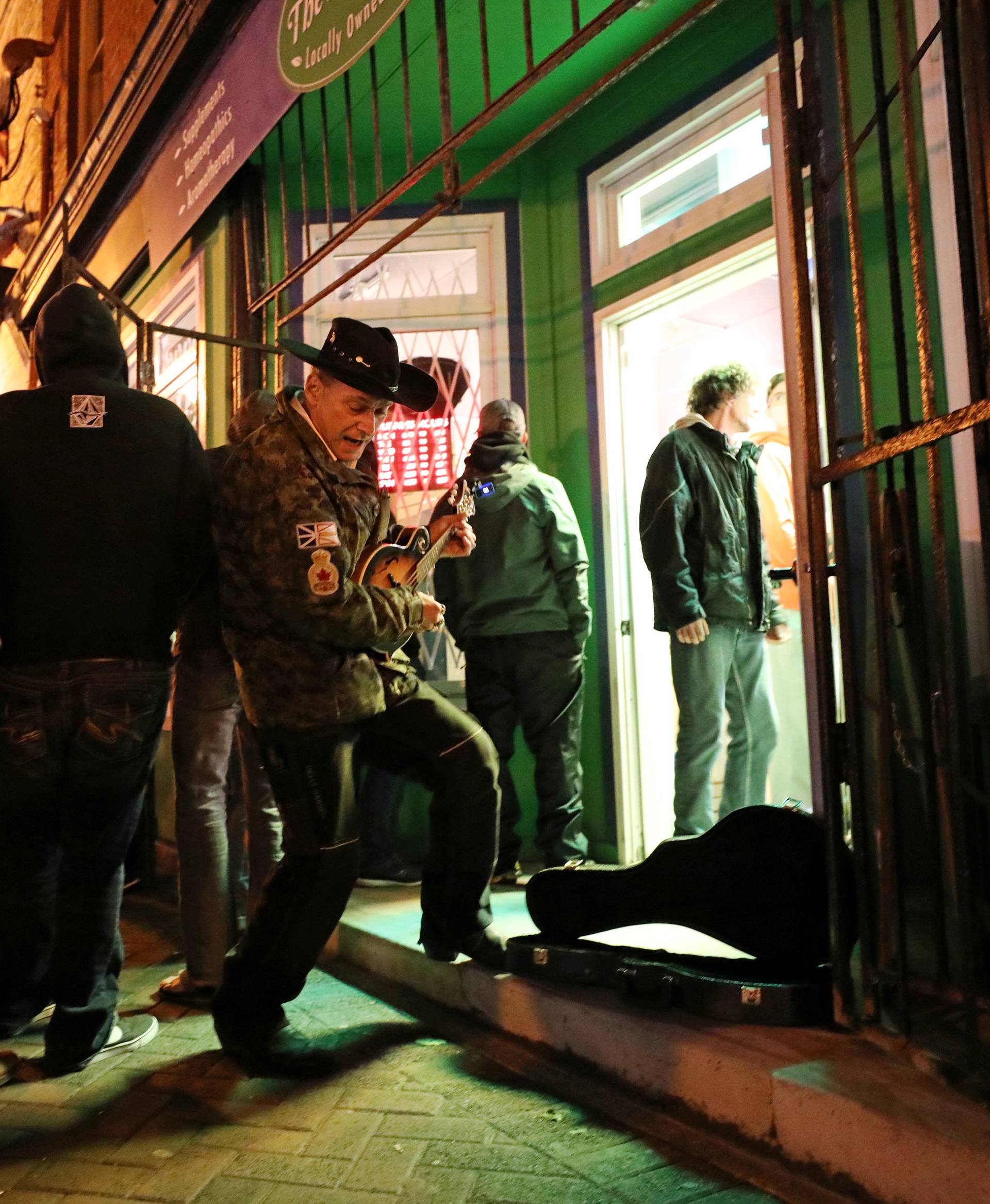 A man plays a song as customers line up outside the Natural Vibe store after legal recreational marijuana went on sale in St John's