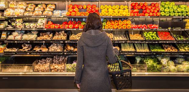 Woman,Standing,In,Front,Of,A,Row,Of,Produce,In