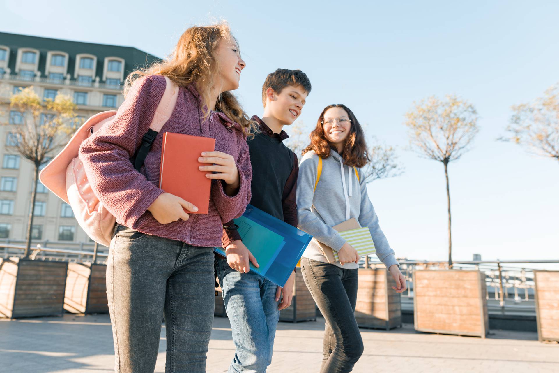 Outdoor portrait of teenage students with backpacks walking and talking. City background, golden hour