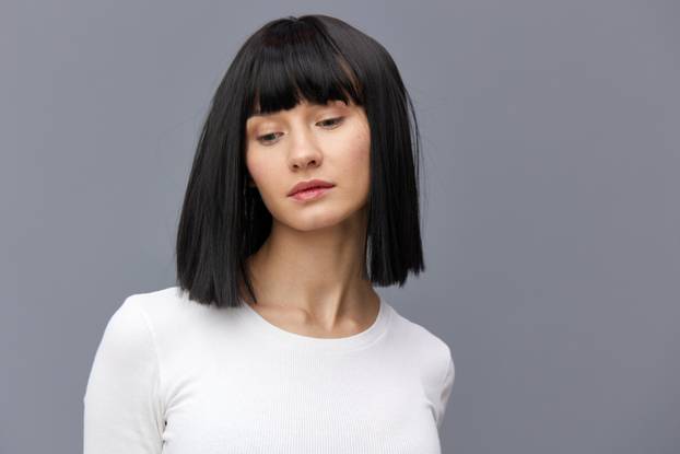 a relaxed woman stands full-face on a dark background in a white tight T-shirt, calmly stands with her hands behind her back