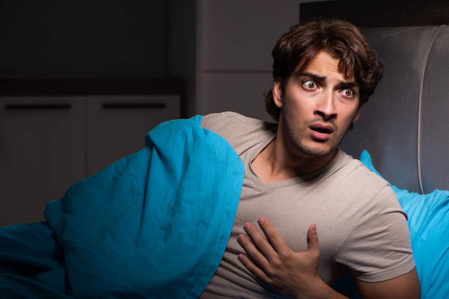 The young man scared in his bed having nightmares