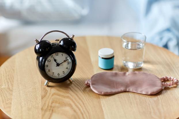 alarm clock, mask and sleeping pills on table