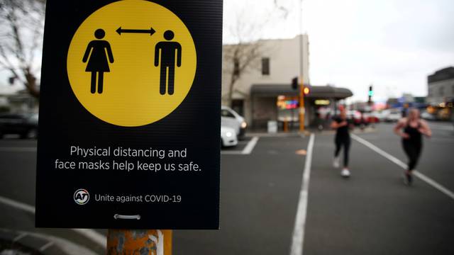 FILE PHOTO: People jog past a social distancing sign in Auckland, New Zealand, August 31, 2020