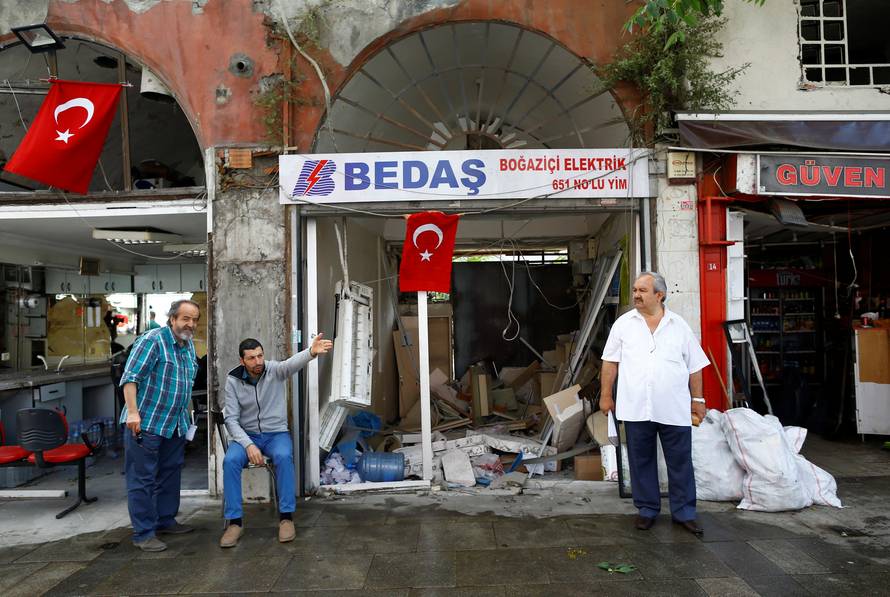 Men sit in front of their damaged shops near the scene of Tuesday's car bomb attack on a police bus, in Istanbul