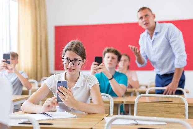 Young students with smartphones sitting in class room