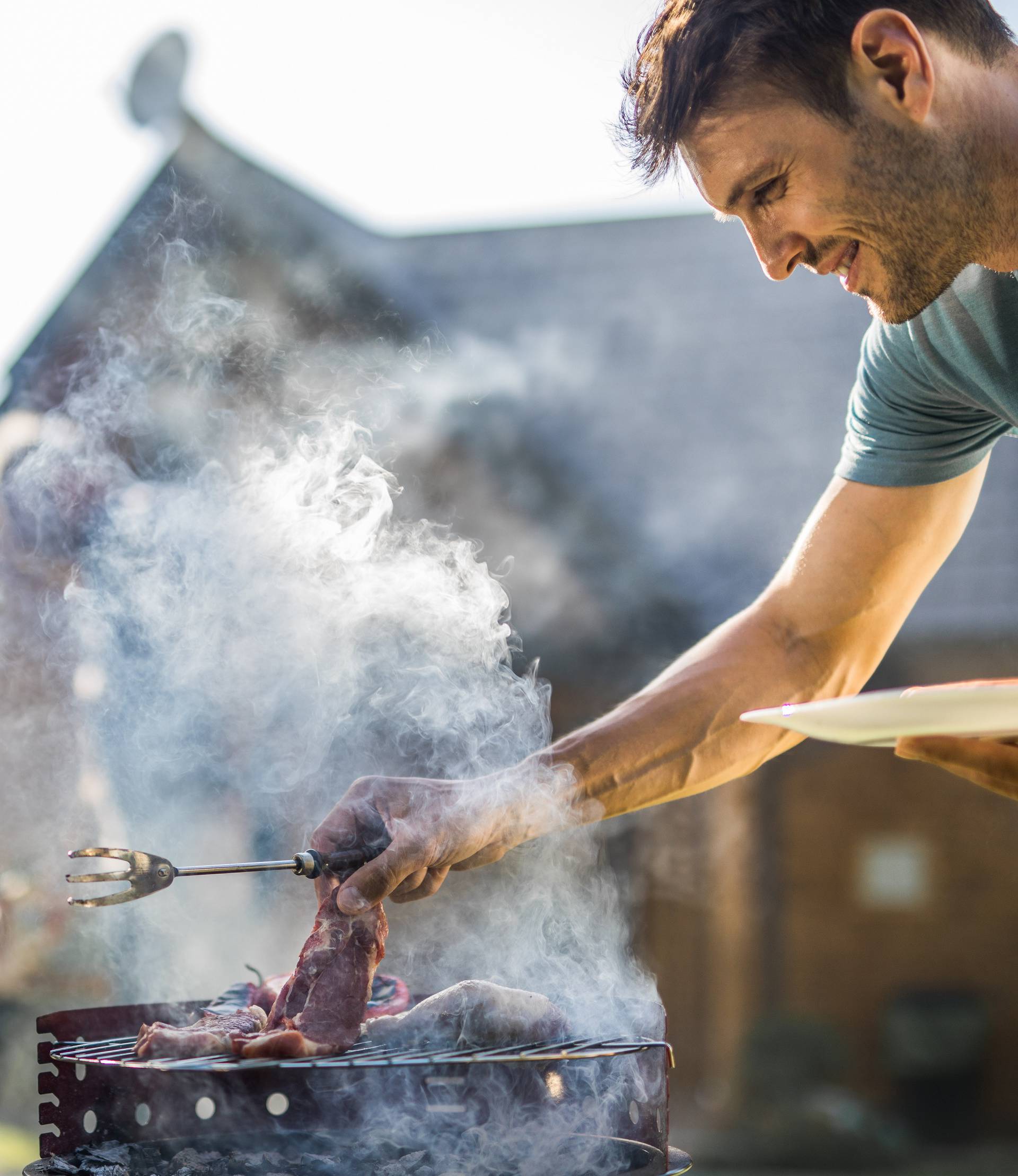 Happy man grilling meat on a barbecue grill outdoors.