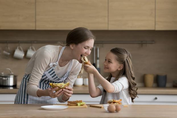 Joyful,Little,Kid,Girl,Giving,Mom,Sandwich,To,Bite.,Happy